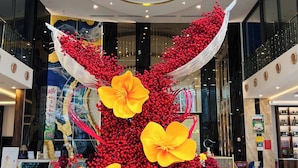 Un vaste atrium agrémenté d’une composition décorative centrale composée de baies rouges et de fleurs jaunes, le tout entouré de rampes de verre et de mobilier moderne.