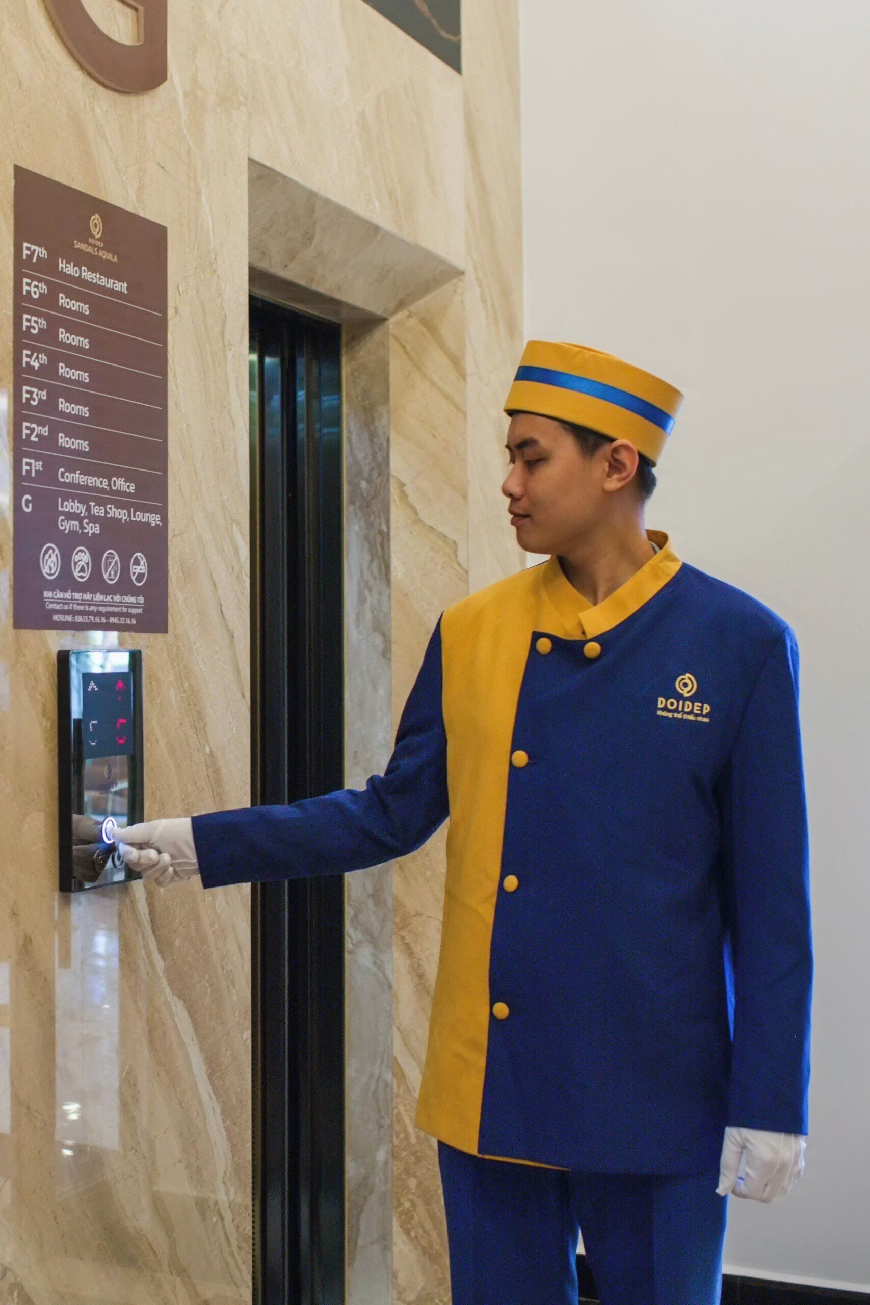 En hotellanställd i uniform som hanterar kontrollpanelen till en hiss.