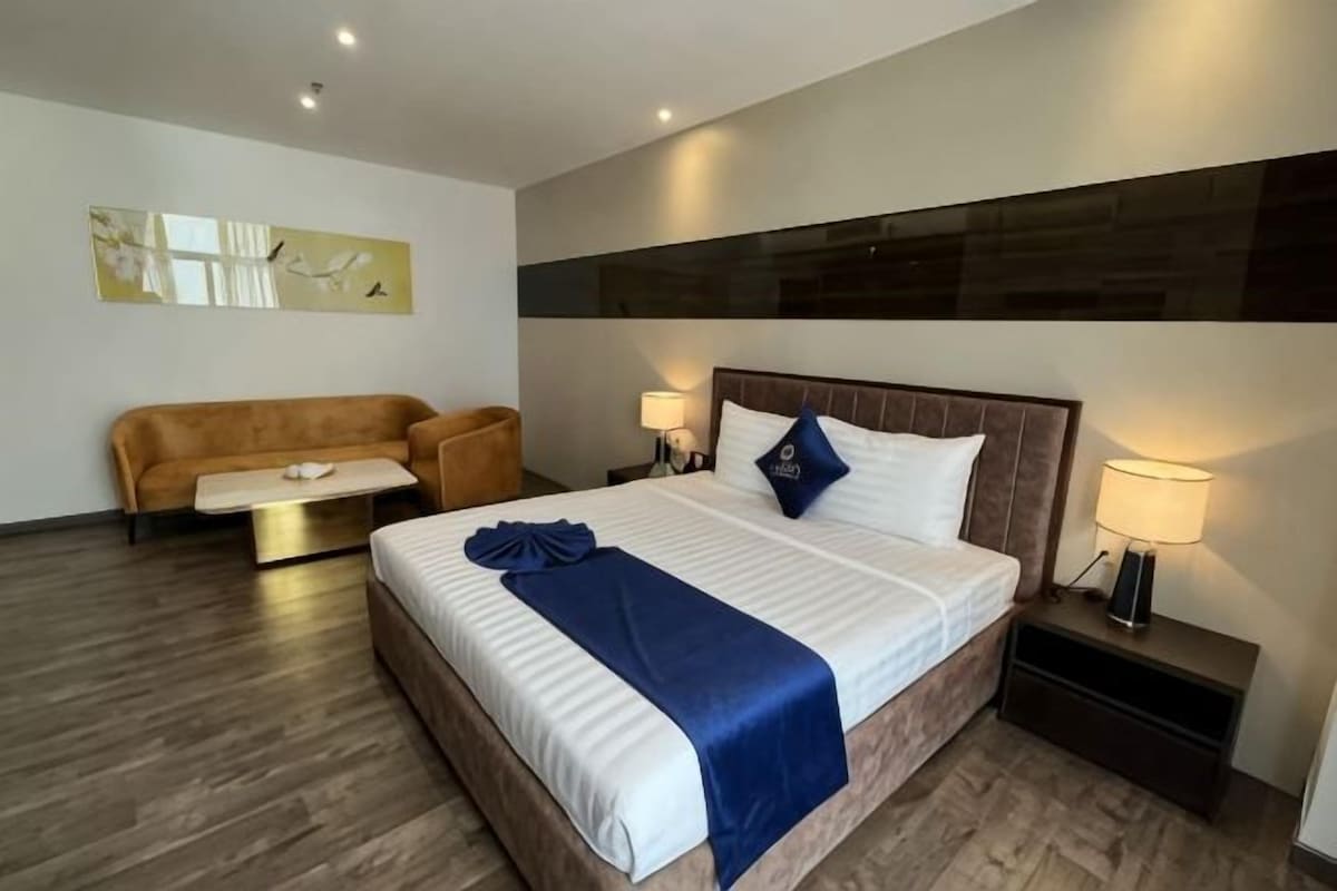 Habitación de hotel con una cama grande, un sofá, una mesita de noche y una obra de arte colgada en la pared.