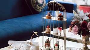 Une table à manger surmontée d’un présentoir à trois niveaux pour les desserts, un vase de fleurs et, au fond, un canapé bleu.