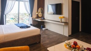 Une chambre d’hôtel avec un lit, un bureau, une télévision et une table à manger avec des fruits.
