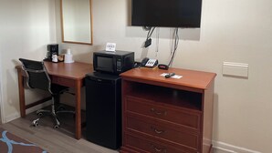 A hotel room with a desk, a chair, a microwave, a coffee maker, a telephone, a clock, and a flat-screen TV mounted on the wall. - American Inn Motel (Pratt)