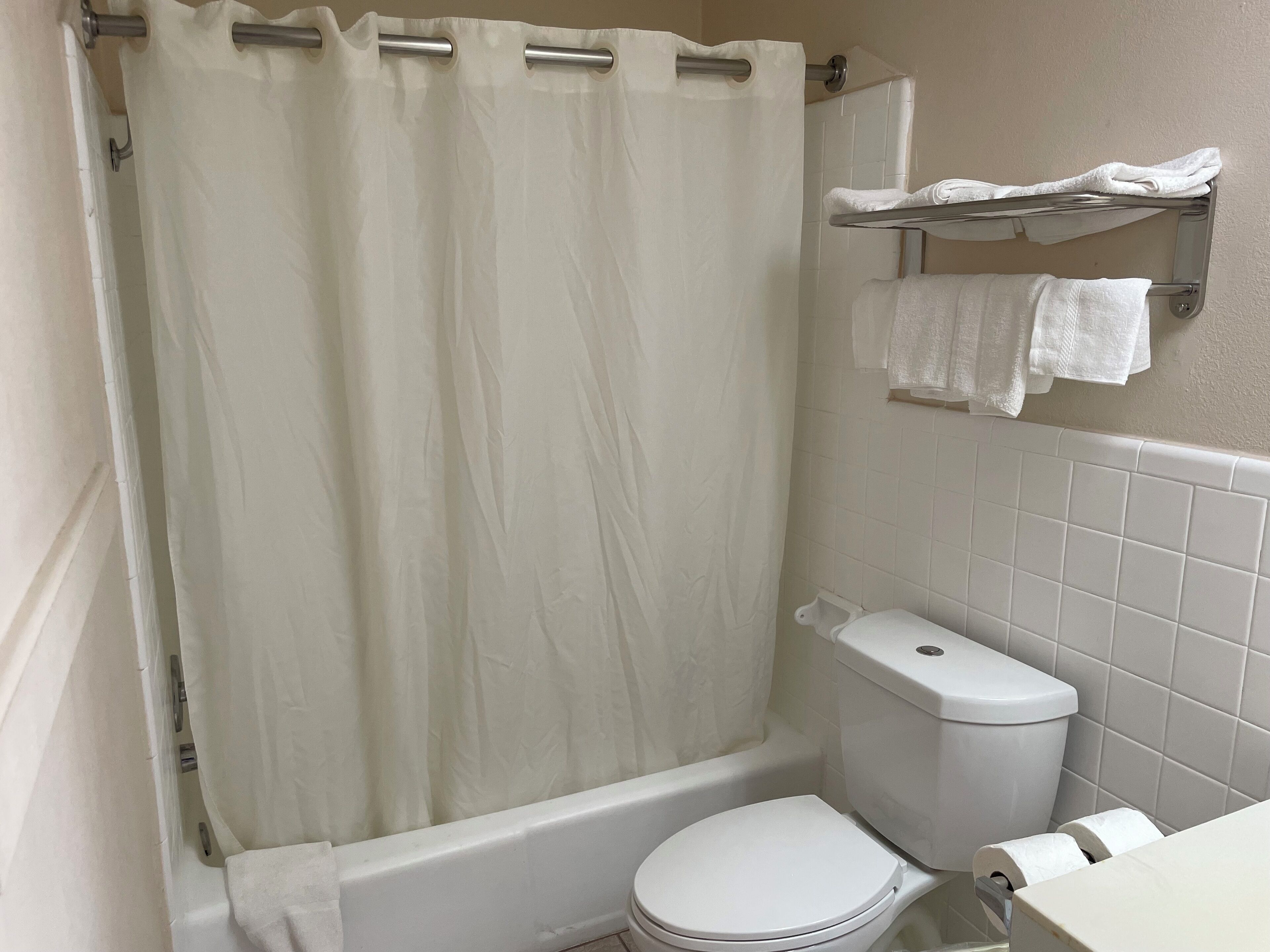 A bathroom with a white shower curtain, a white toilet, and a towel rack with towels.