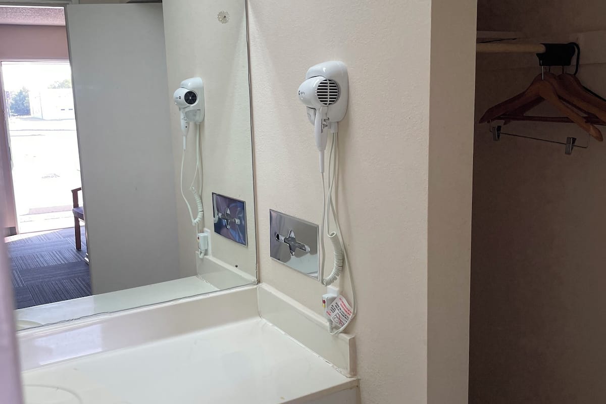 A bathroom with a white sink, a mirror, and two wall-mounted hair dryers.