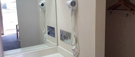 Un baño con un lavamanos blanco, un espejo y dos secadores de pelo fijados a la pared.
