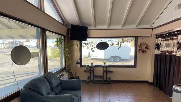 A room with a large window, a blue sofa, a small table with plants, and a speaker mounted on the wall. - American Inn Motel (Pratt)