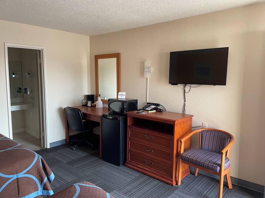Habitación de hotel con escritorio, silla, televisor, microondas, cafetera y minibar.