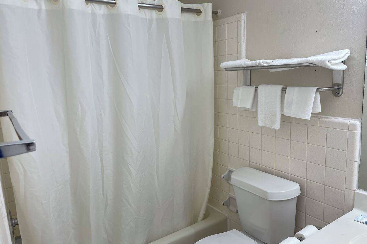 A bathroom with a shower curtain, a toilet, a towel rack with towels, and a tiled wall.