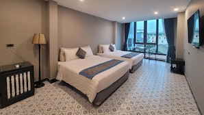 Quarto de hotel com duas camas, uma escrivaninha, uma cadeira e uma janela grande com vista para a cidade.