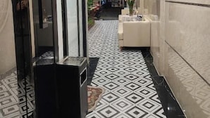 Um saguão de hotel com piso de padrão geométrico, um balcão de recepção e uma área de estar com um vaso de flores.