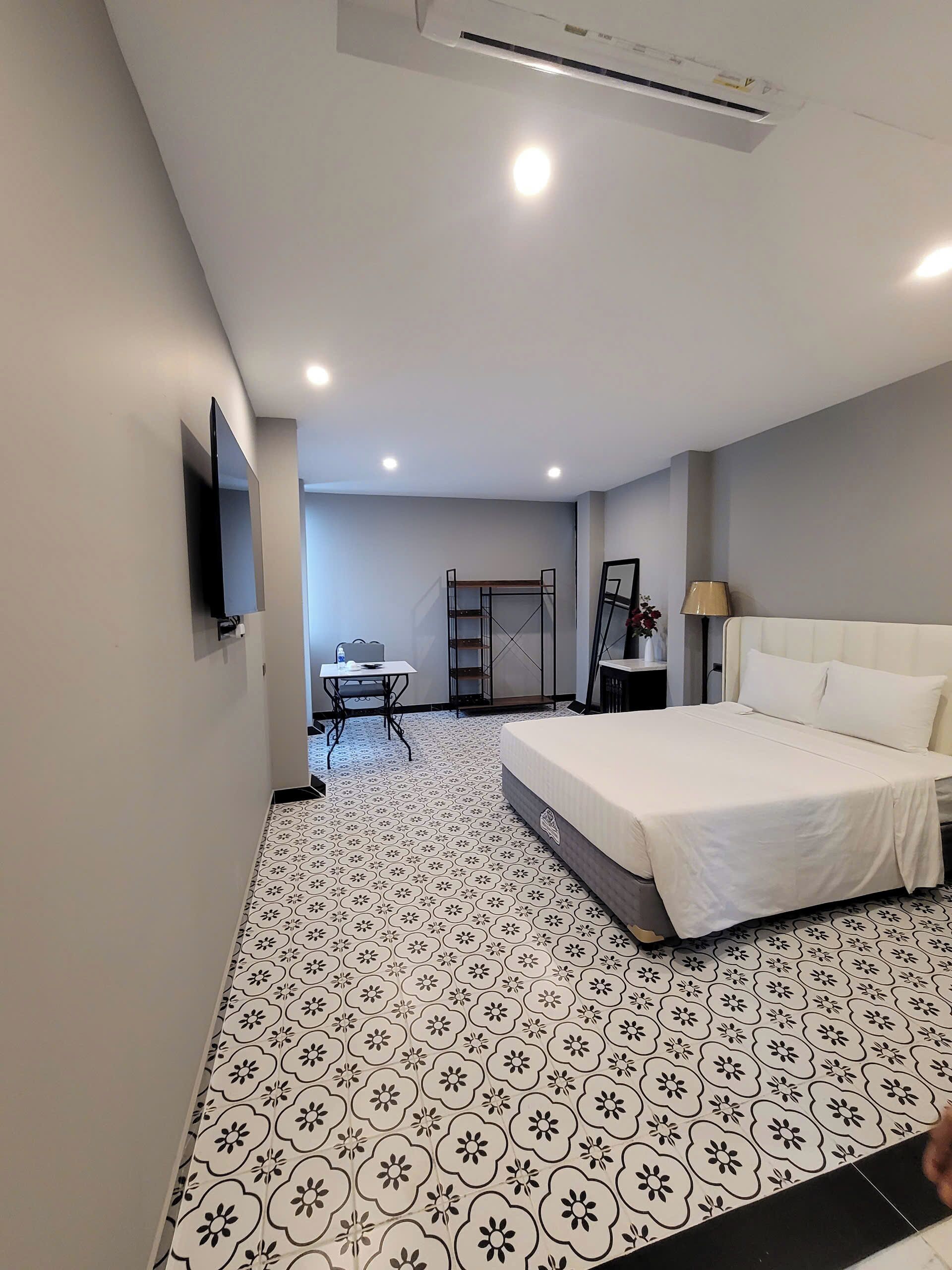 A hotel room with a bed, a desk, a chair, a TV, and a lamp.