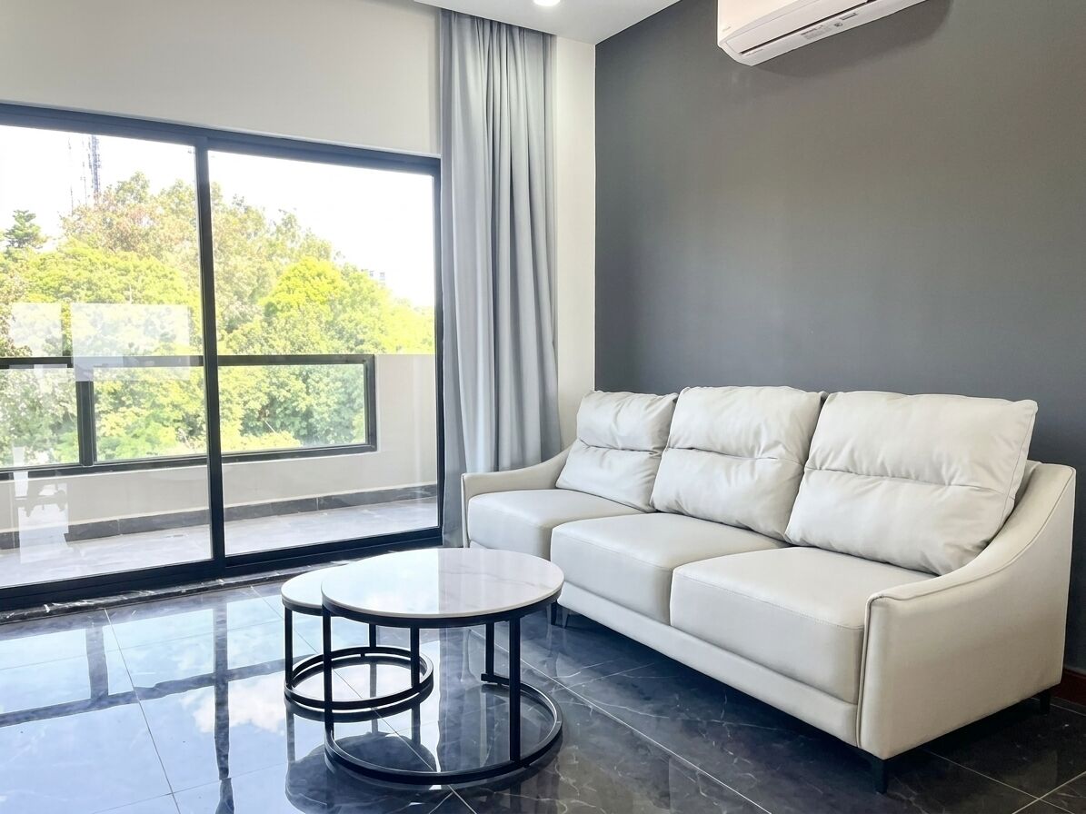 A modern living room with a white leather sofa, a round coffee table, and a large window with a view of greenery.
