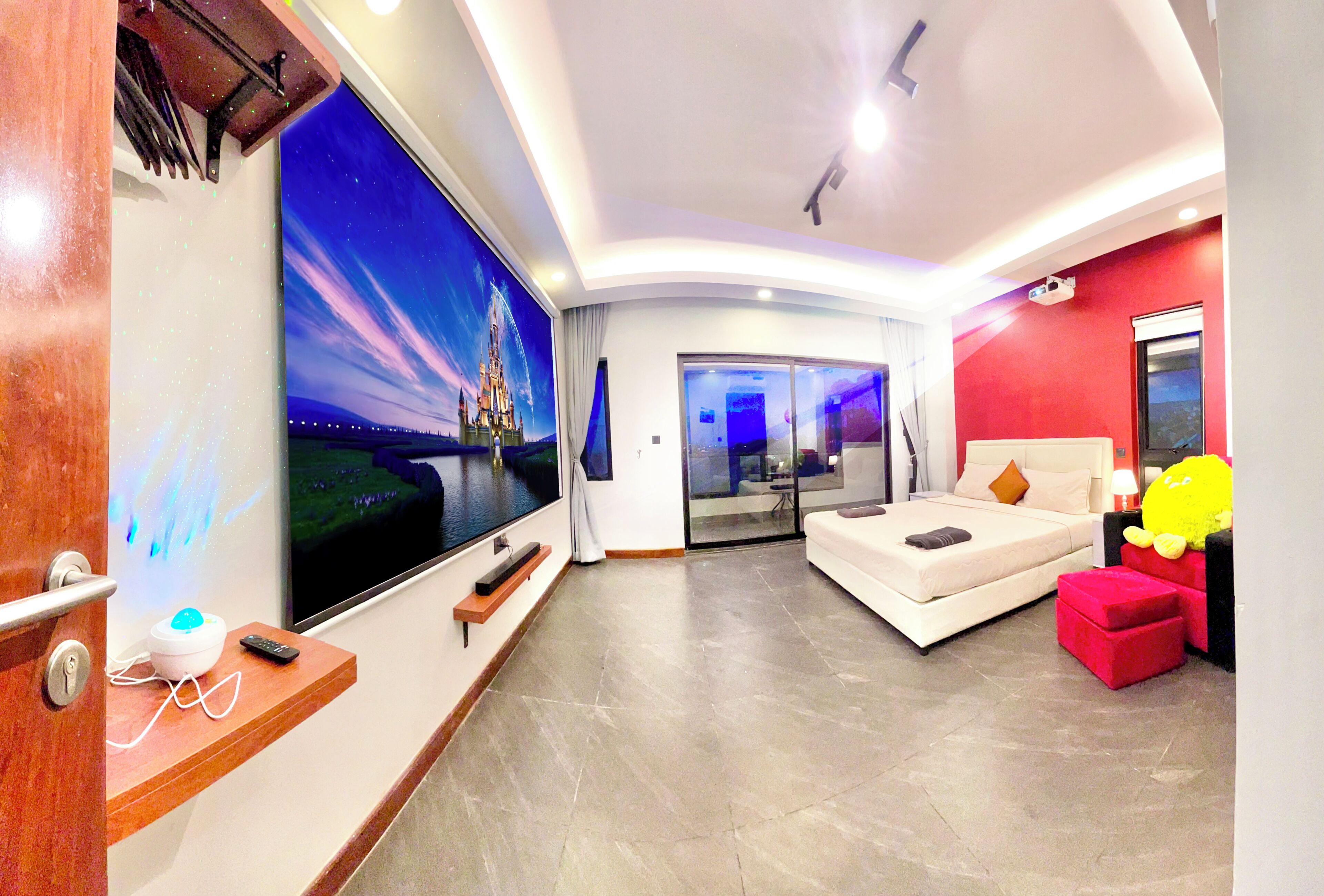 A modern hotel room with a large flat-screen TV, a bed, a seating area, and a view of a castle through the window.