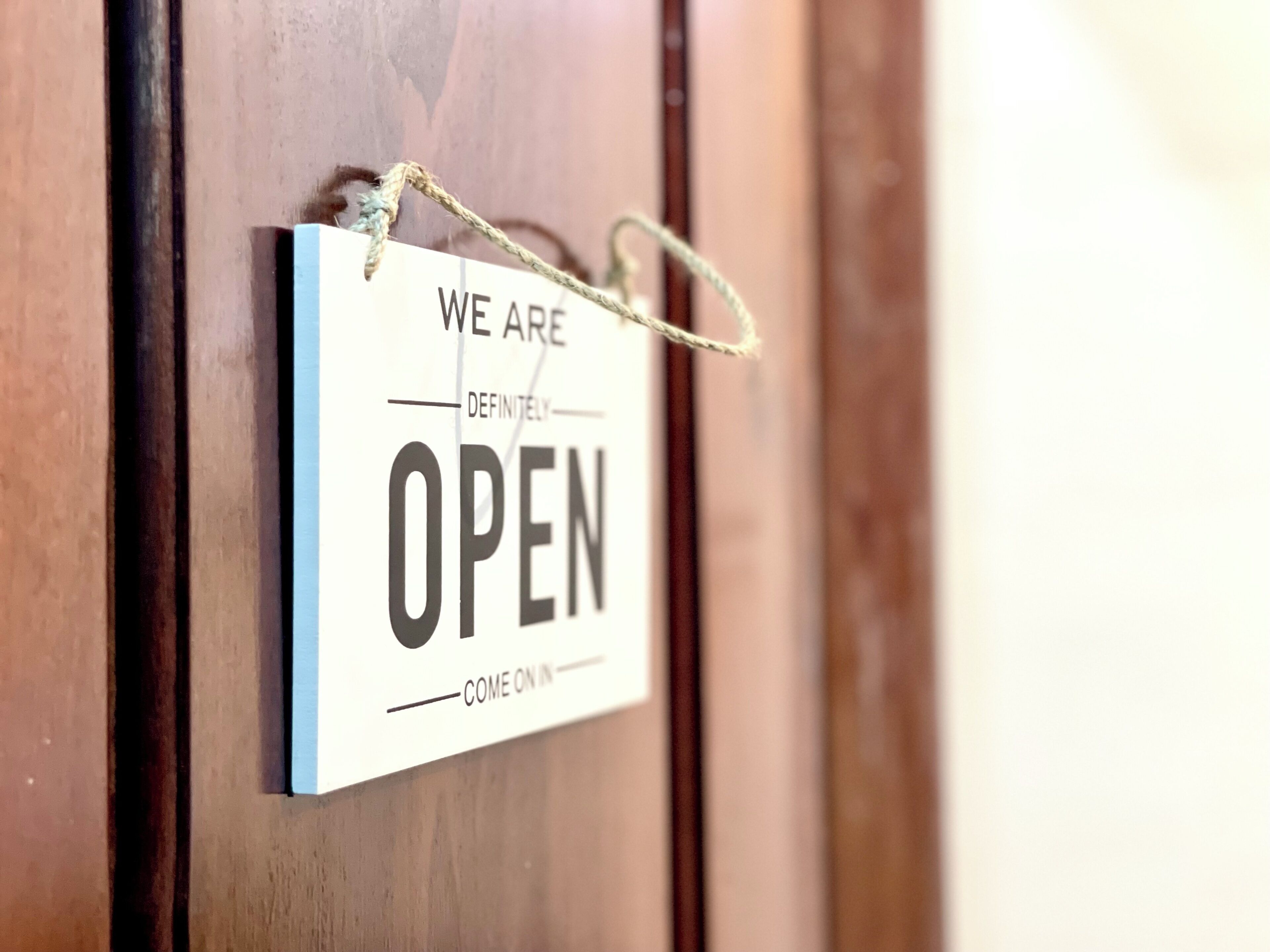 Ein Schild mit dem Text 'WE ARE DEFINITELY OPEN COME ON IN' hängt an einer Holztür.