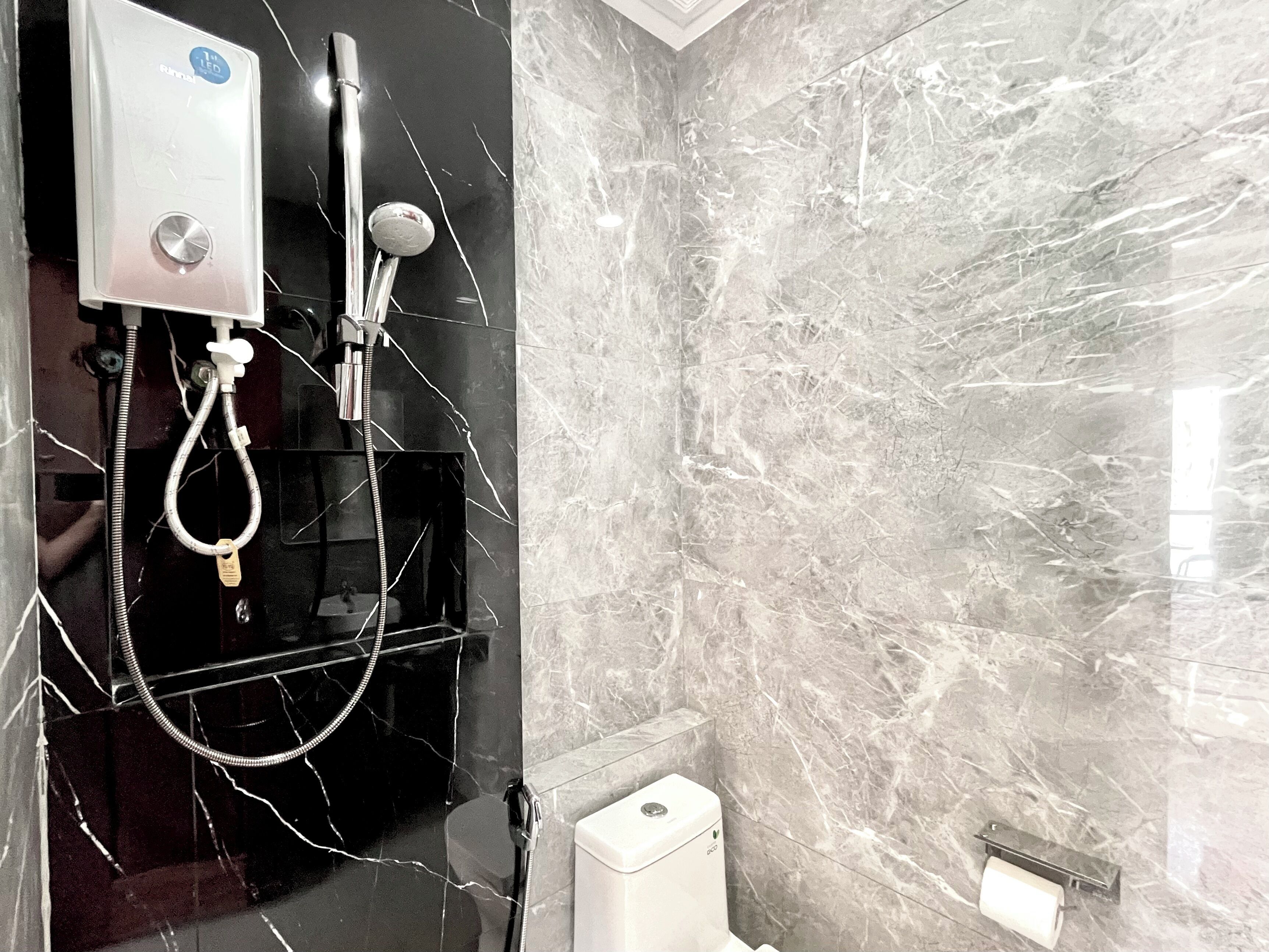 Un baño con pared de mármol, ducha con cabezal de ducha manual y un inodoro.