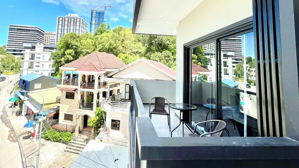 A modern building with a balcony featuring a glass table and chairs, overlooking a cityscape with various buildings and a construction crane.