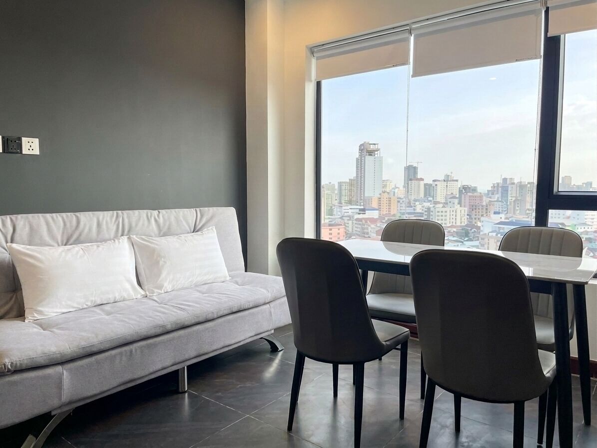 A modern living room with a grey sofa, two black chairs, and a dining table. A large window offers a city view.