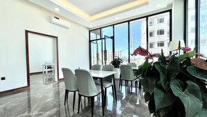 A modern dining area with a large table and chairs, large windows with a city view, and a potted plant.