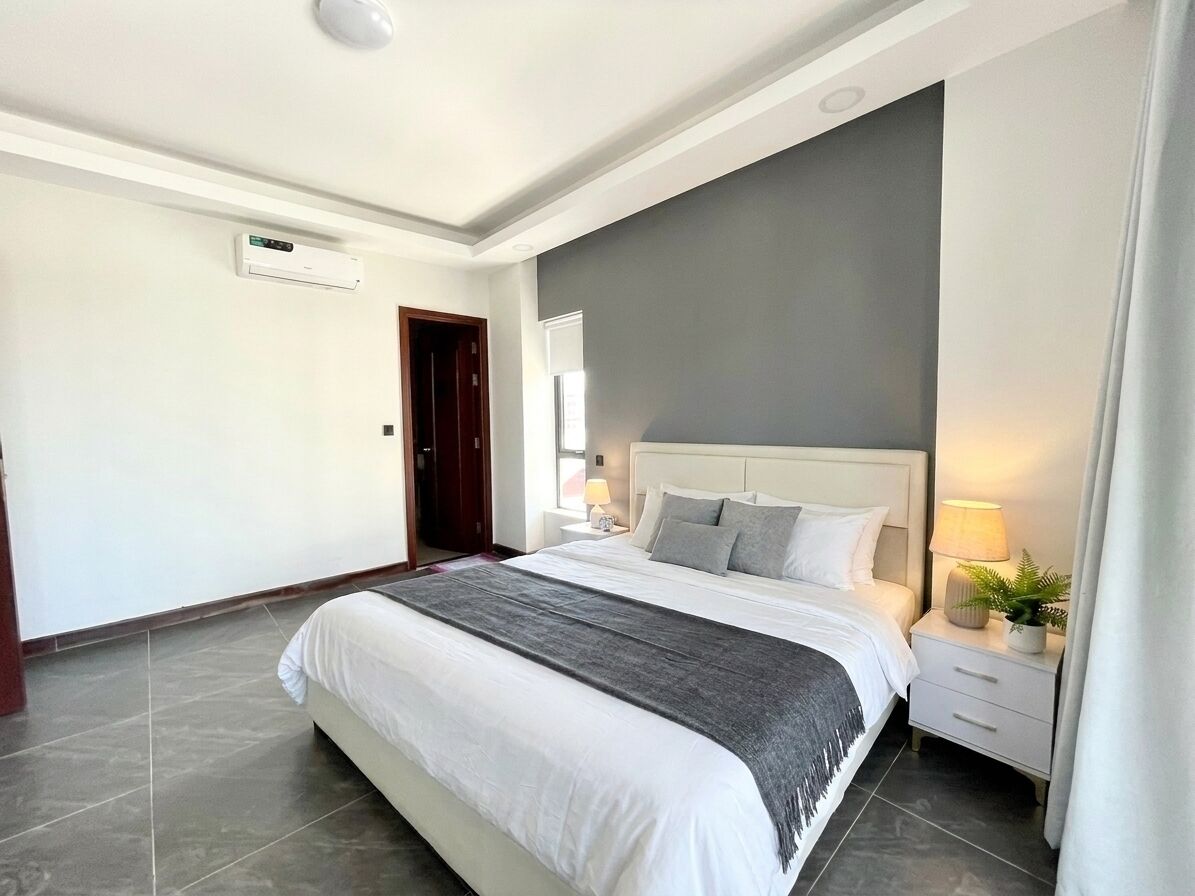 A modern hotel room with a large bed, a bedside table with a lamp, and an air conditioning unit on the wall.