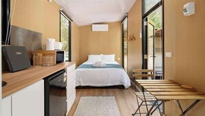 Habitación de hotel pequeña con cama, escritorio con computadora portátil, kitchenette y ventana grande con vistas al exterior.