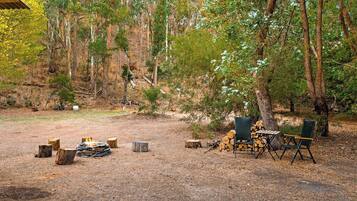 An outdoor camping area with a fire pit, chairs, and a table.