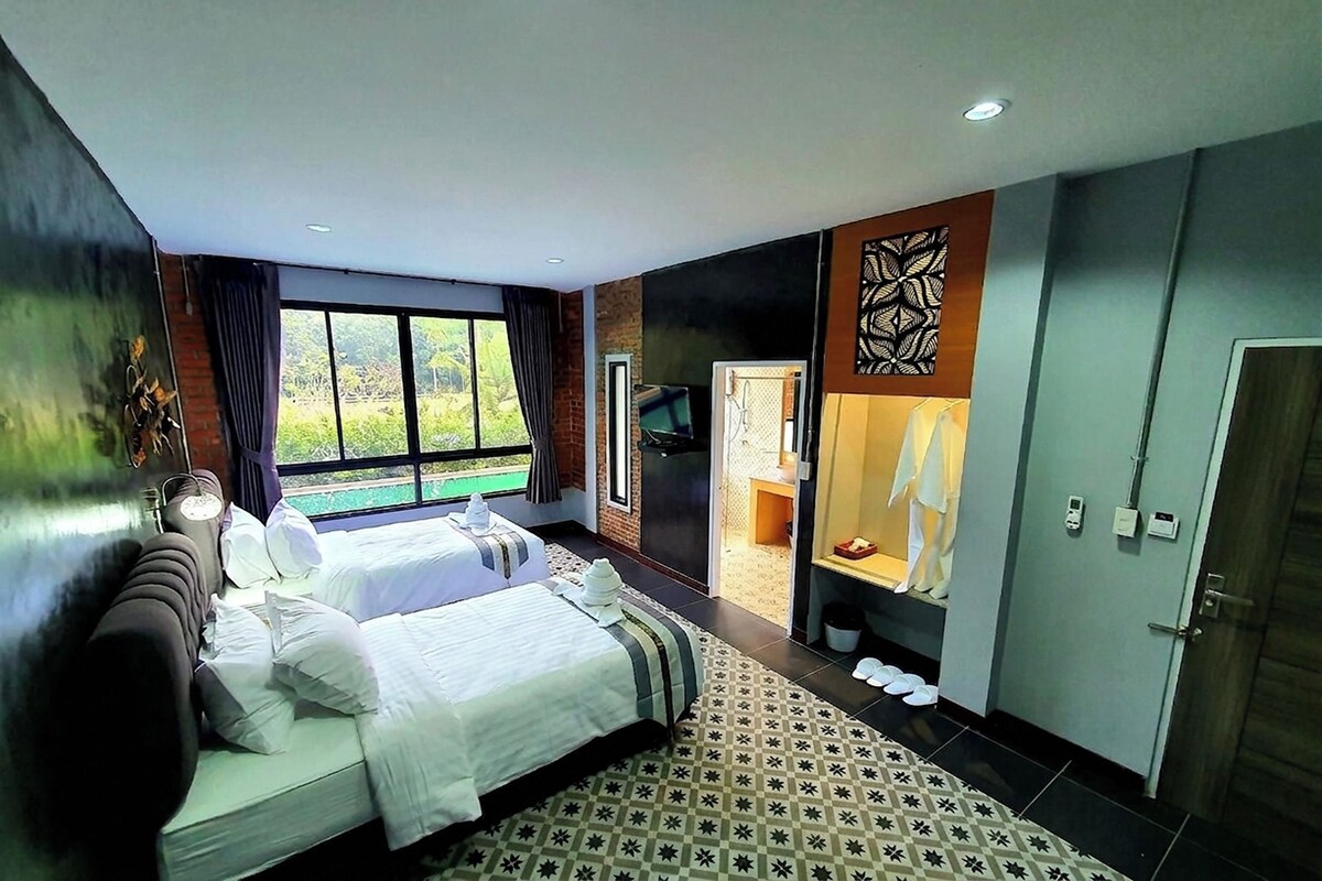 A hotel room with a large bed, a view of greenery outside, and a bathroom with a shower and toilet.