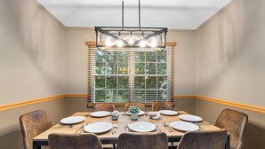 Uma sala de jantar com uma mesa posta para seis pessoas, seis cadeiras, um candelabro e uma janela com persianas.