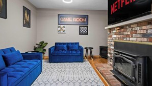 Sala de estar com lareira, sofá azul, placa indicando sala de jogos e uma televisão exibindo 'NETFLIX'.