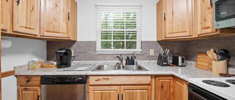 A kitchen with wooden cabinets, a dishwasher, a coffee maker, a toaster, and a window with blinds.