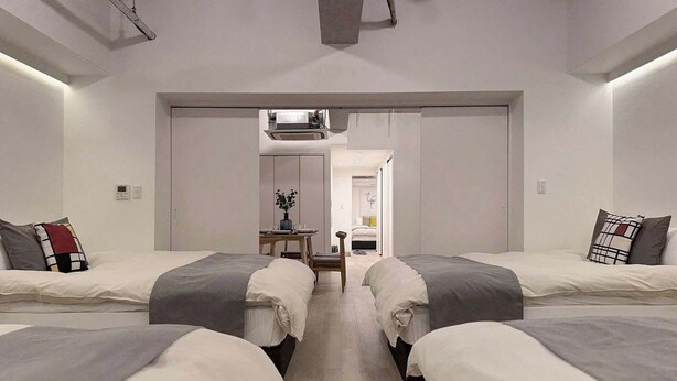 A modern hotel room with two single beds, a small table with a vase, and a view of the hallway. - Spacious 2BR Apt in Hatchobori for Up to 10 Guests (Hiroshima)