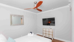 A bedroom with a bed, a ceiling fan, a TV, a dresser, and a mirror.