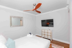 Une chambre à coucher comprenant un lit, un ventilateur de plafond, une télévision, une commode et un miroir.