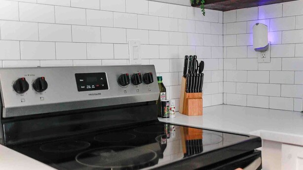 A kitchen with a stainless steel stove, a knife block, and a white tiled backsplash.