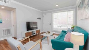 A modern living room with a teal sofa, a TV on a white stand, a small white table, and a lamp.
