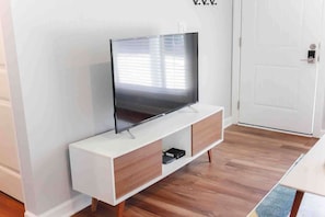 Un salon moderne avec un téléviseur à écran plat posé sur un meuble blanc, un parquet en bois et une porte blanche en arrière-plan.