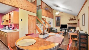 Un vaste espace de vie agrémenté d’un escalier en bois, d’une cheminée et d’une table à manger avec des chaises.
