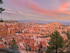 A panoramic view of a rugged canyon landscape with distinctive red rock formations and sparse vegetation.
