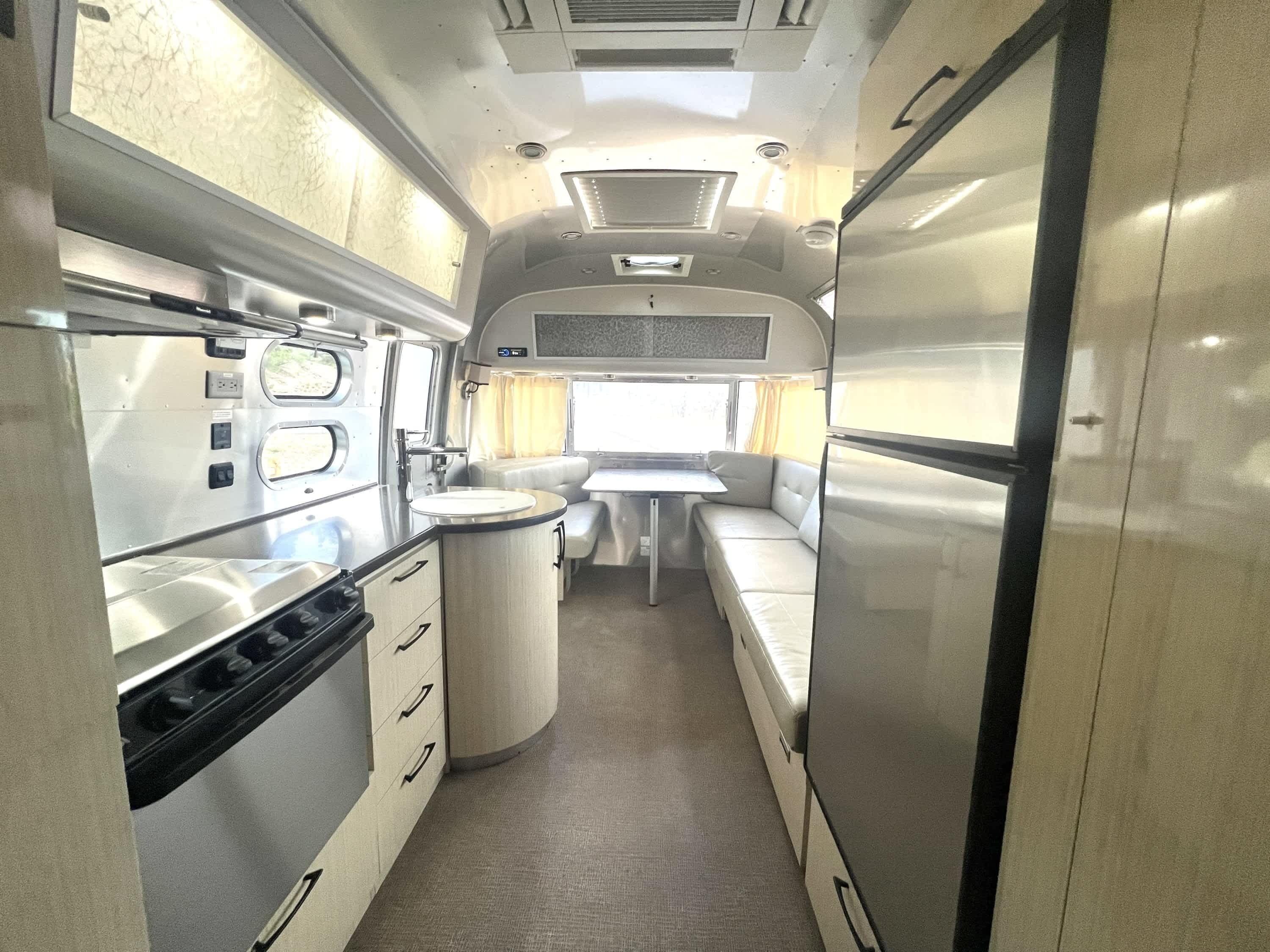 A compact RV interior with a kitchenette, a dining area, and a small bathroom.
