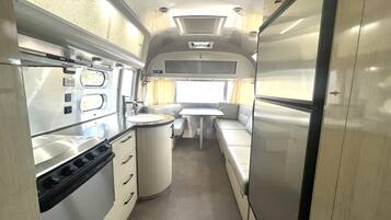 A compact RV interior with a kitchenette, a dining area, and a small bathroom.