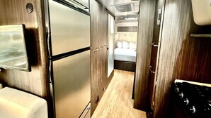 A narrow corridor with a refrigerator, a stove, and a bed in the background. - Airstream near Zion & Bryce with Pools (Orderville)