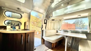 A compact RV interior with a kitchenette, a seating area, and a window offering a view of the outside. - Airstream near Zion & Bryce with Pools (Orderville)