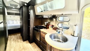 A compact kitchen with a stove, sink, and a small countertop area. - Airstream near Zion & Bryce with Pools (Orderville)