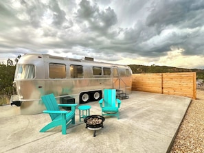 A silver trailer with a patio area featuring turquoise chairs and a small table.