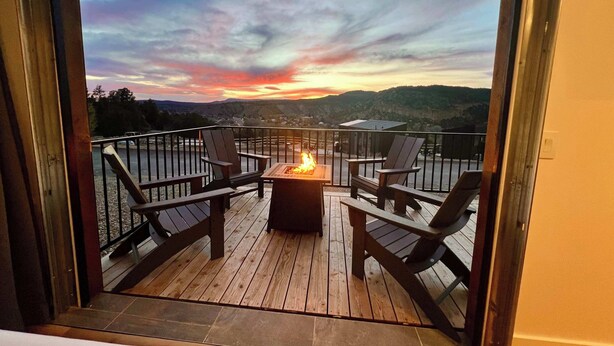 Eine Terrasse mit Feuerstelle und Stühlen, mit Blick auf eine malerische Landschaft mit Bergen und Sonnenuntergang.