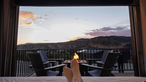 Ein Balkon mit Stühlen und Tisch, der auf eine gebirgige Landschaft blickt.