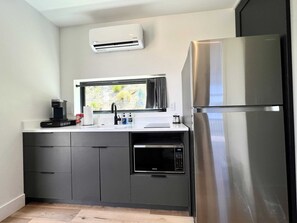 Una cocina moderna con microondas integrado, refrigerador de acero inoxidable y ventana con vista a follaje.