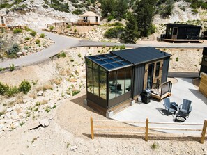 A modern glass structure with a solar panel roof, a barbecue area, and a small deck with chairs.