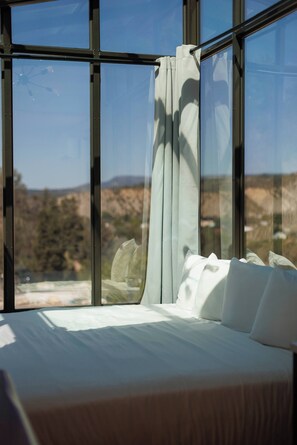 A bed with white bedding, a window with a view of a landscape, and a curtain partially drawn.