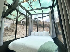 Ein Zimmer mit einem Bett, großen Fenstern und Blick auf eine felsige Landschaft.
