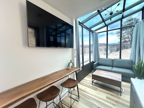 A modern living room with a large window, a sofa, a coffee table, and a bar area with stools. - Stargazing cabin near Bryce & Zion w/resort pools (Orderville)